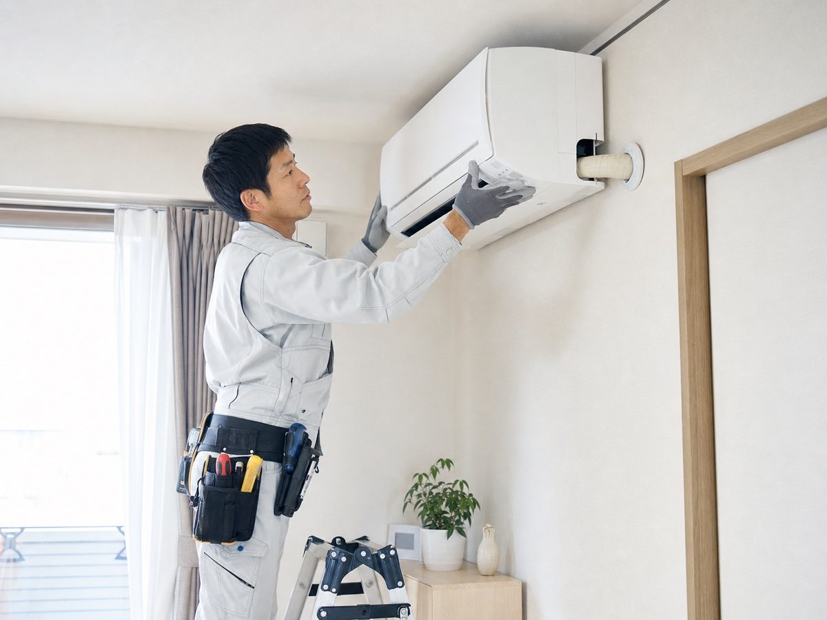 住宅の壁掛けエアコンを点検する職人（AI・構成見本）